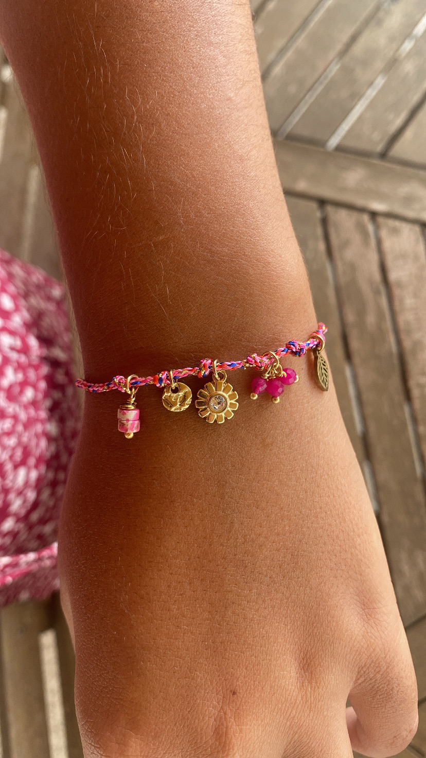pulseira trançada rosa com pendentes dourados e pedras rosas no pulso