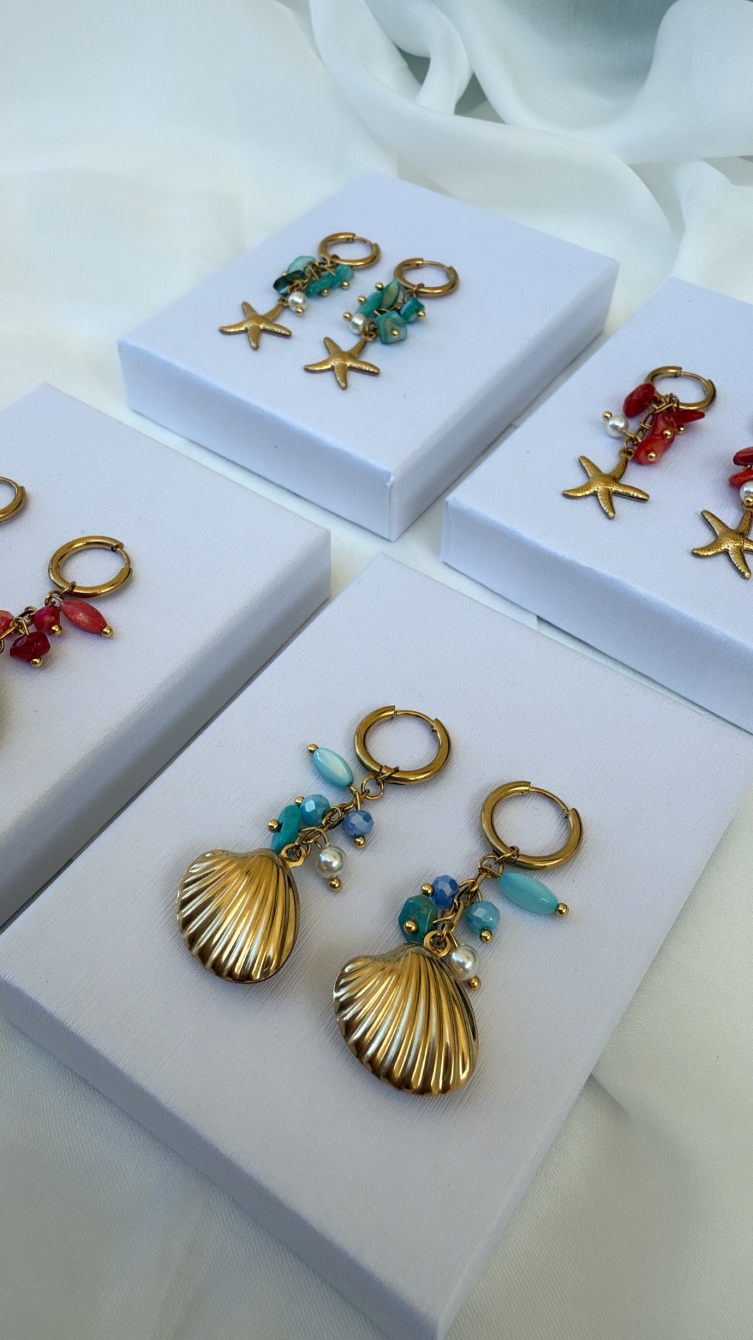 Brincos dourados com pingentes de estrela-do-mar e concha em suportes brancos.