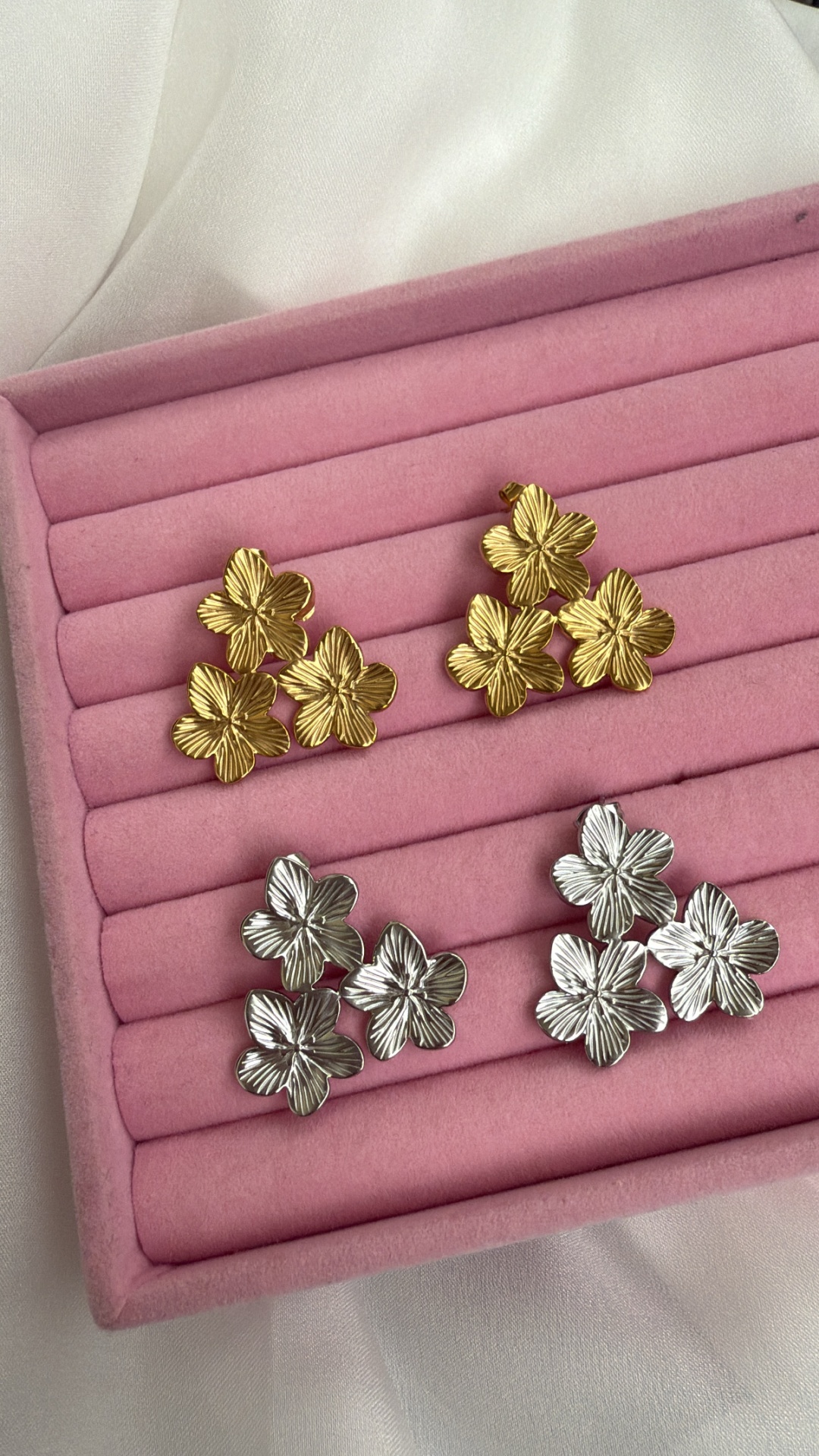Brincos florais dourados e prateados numa caixa de veludo rosa