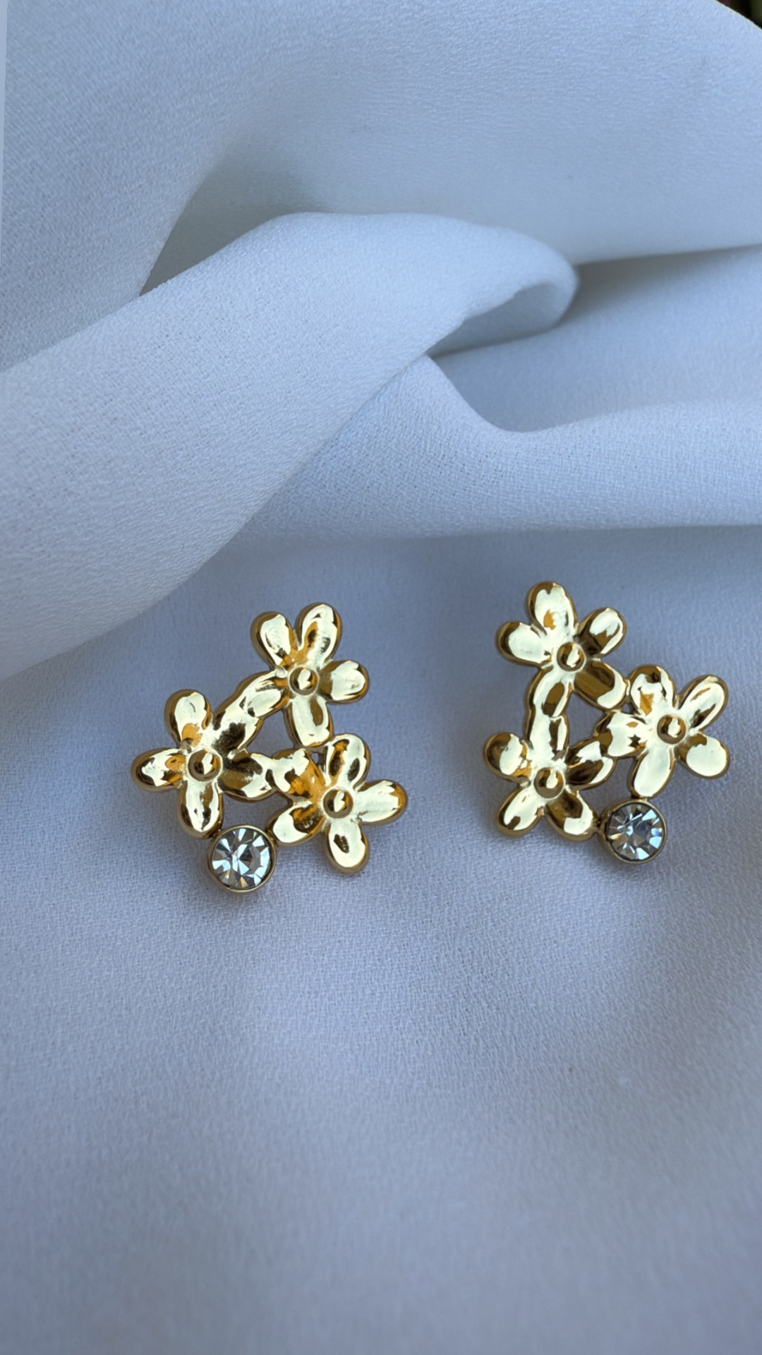 Brincos dourados em forma de flores com pedras brilhantes sobre tecido branco