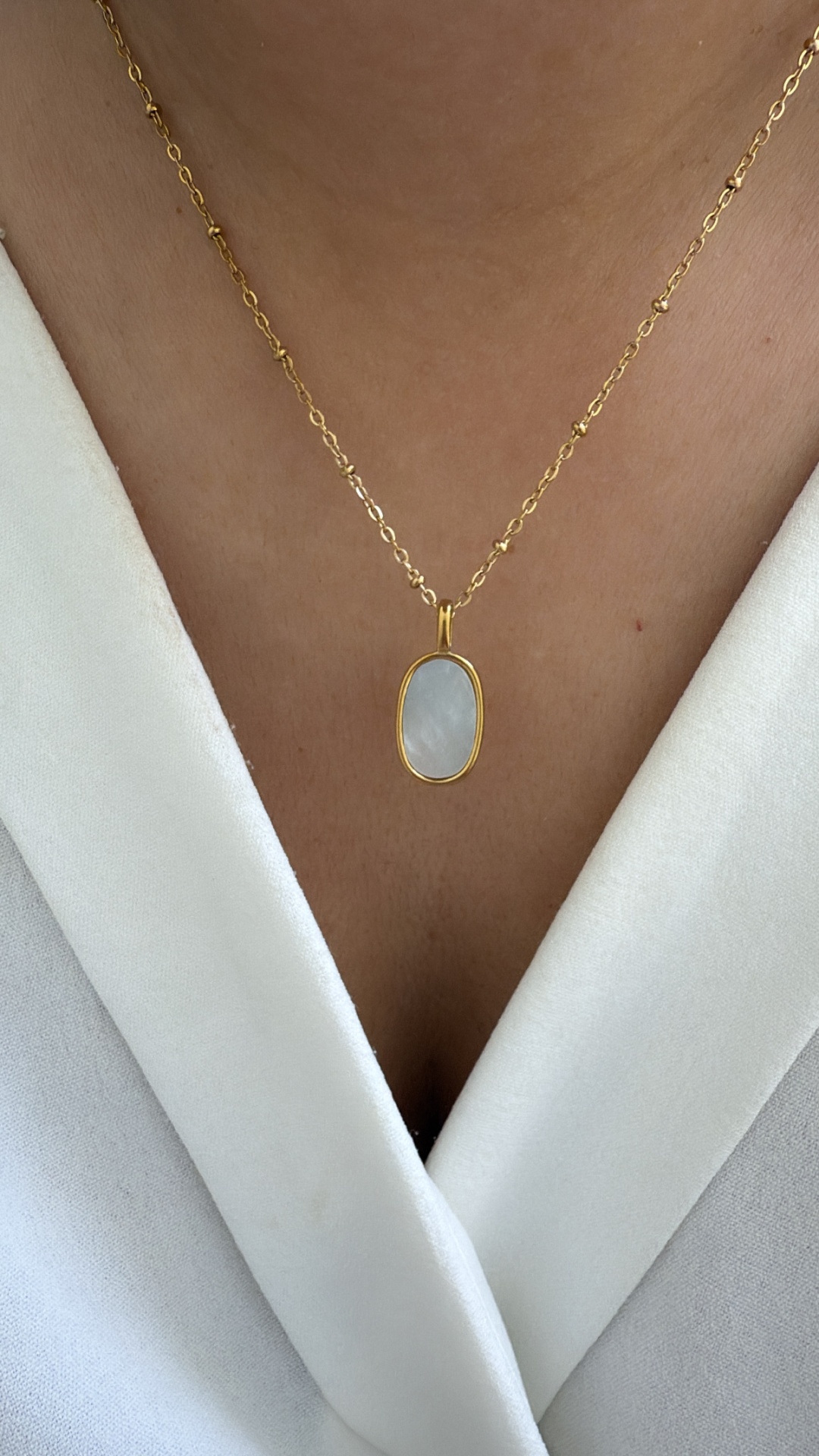 Colar dourado com pendente oval branco usado com blusa branca