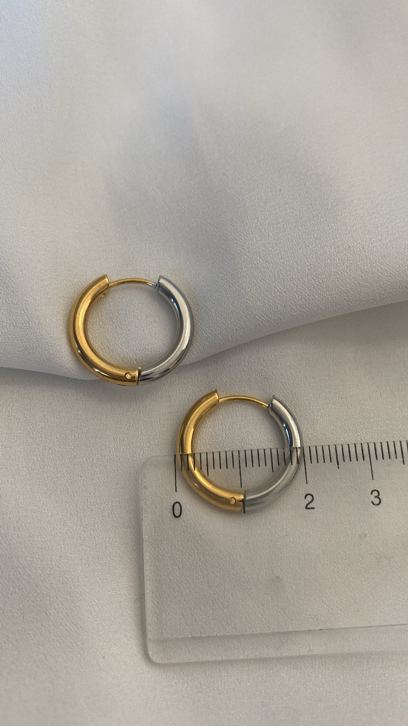 Brincos de argola bicolor dourado e prateado sobre tecido branco com régua