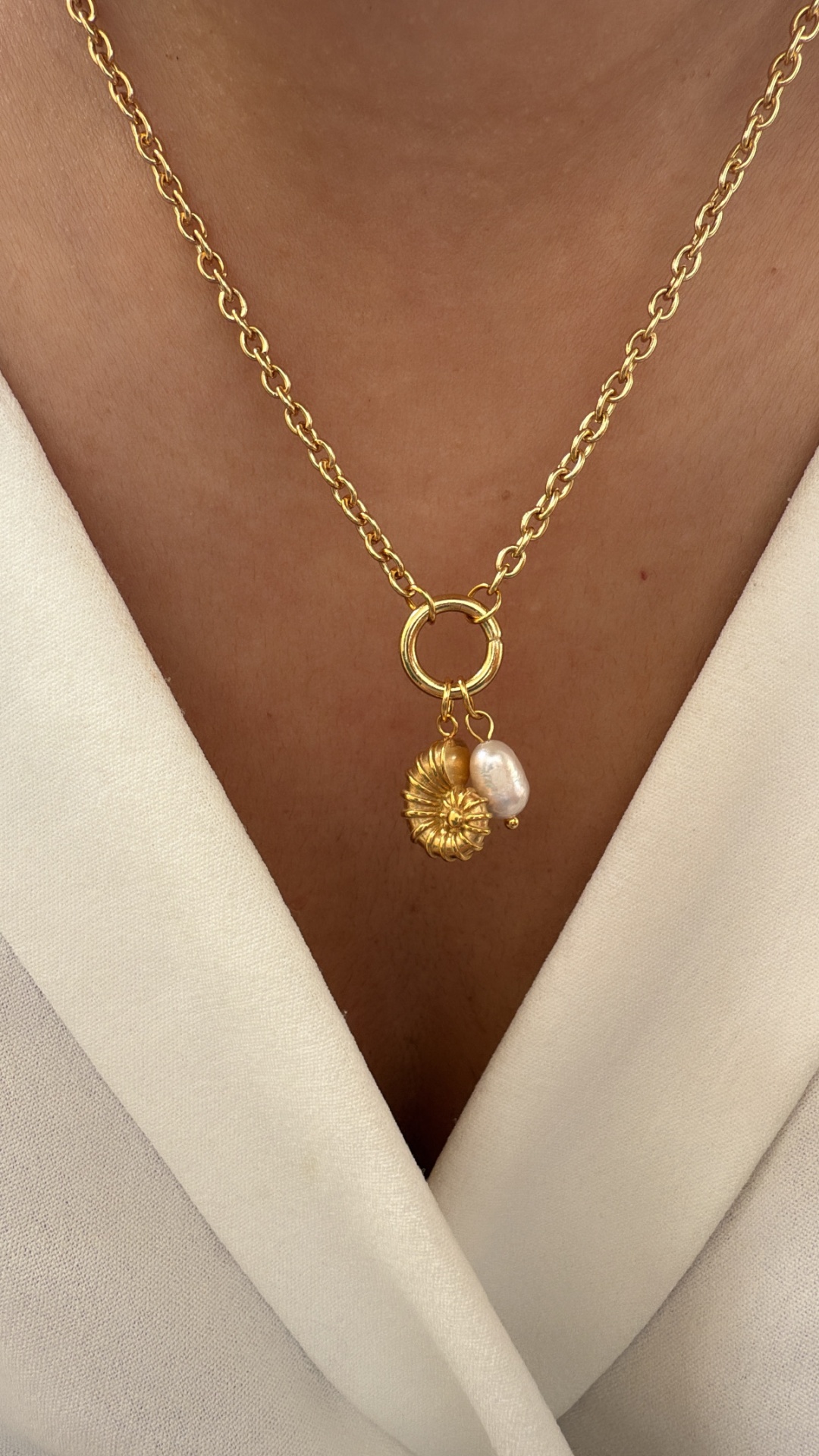 Colar dourado com pingente de flor e pérola em pele morena e roupa bege clara