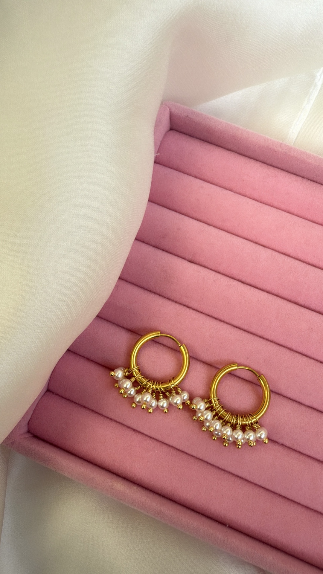 Brincos dourados com bolas brancas numa almofada rosa