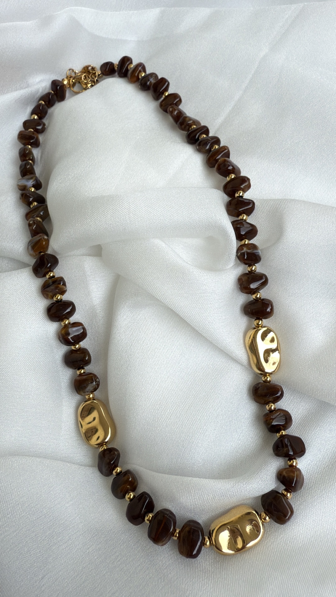 Colar de pedras castanho-escuro e contas douradas sobre tecido branco