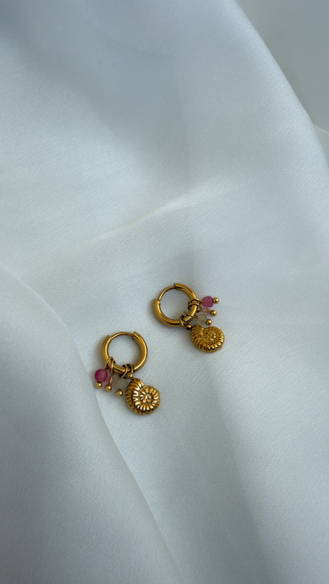 Brincos dourados com pendentes circulares e contas rosa e brancas sobre tecido branco