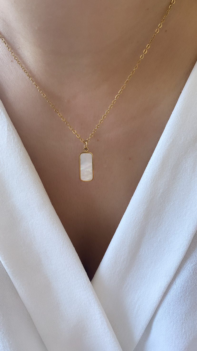 Colar dourado com pendente retangular de madrepérola em pescoço sobre roupa branca