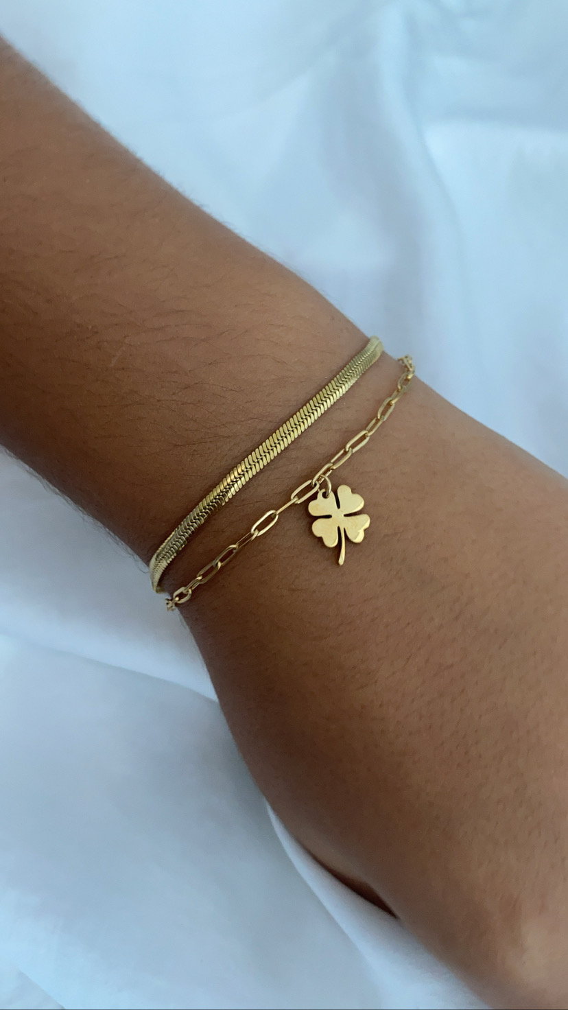 Pulseira dourada com trevo de quatro folhas num fundo branco
