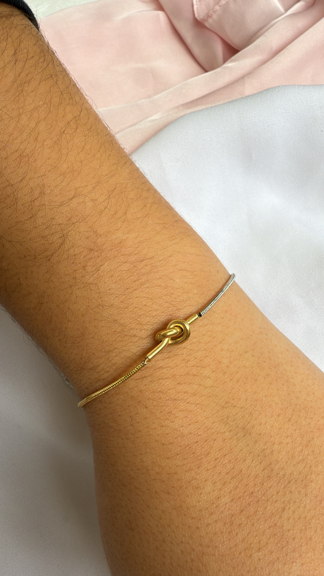 Pulseira fina dourada e prateada com nó dourado no pulso