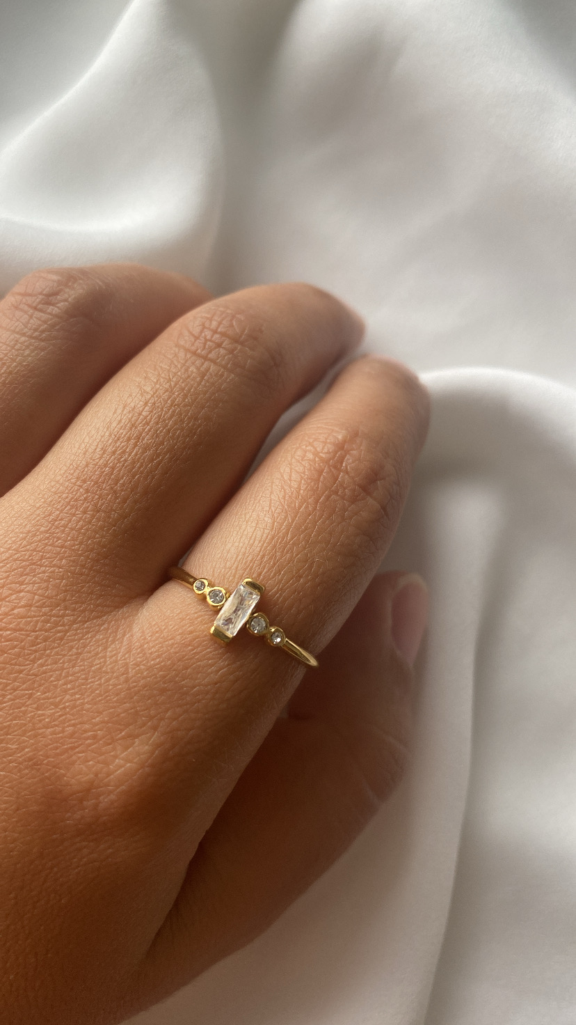 Anel dourado com pedras numa mão sobre tecido branco