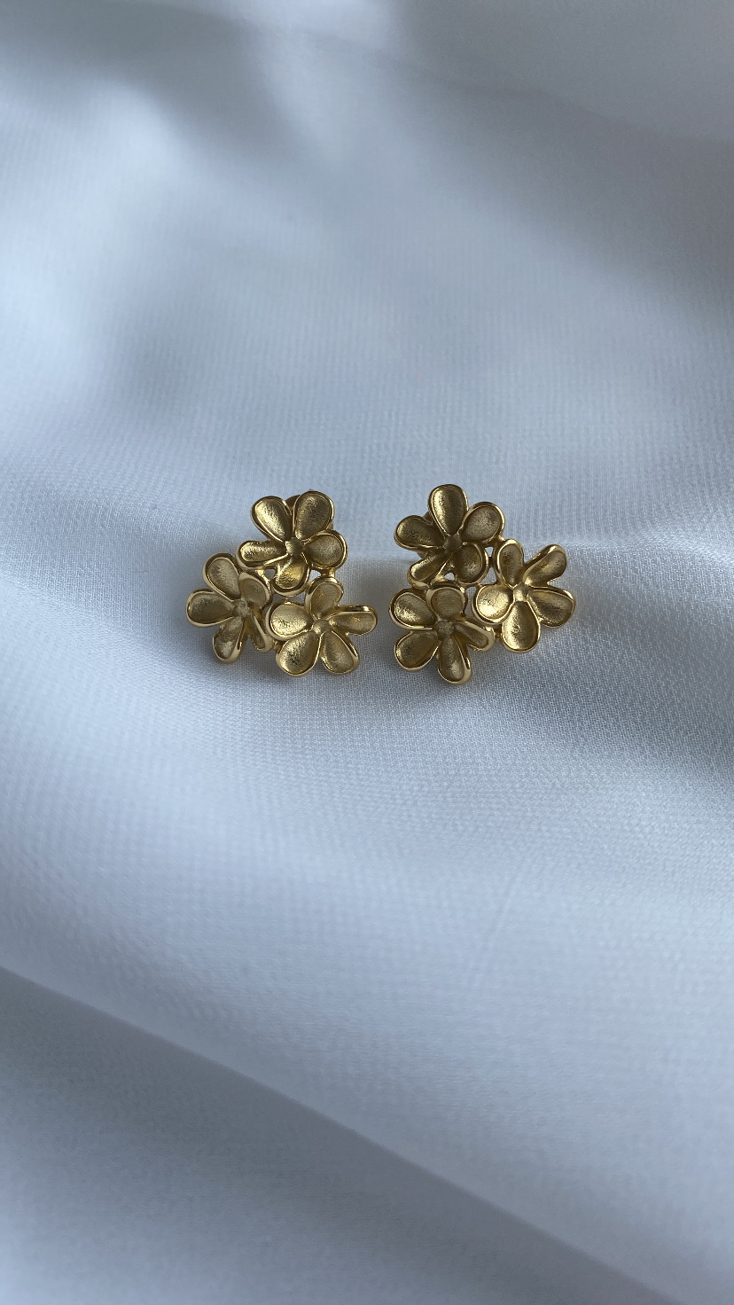 Brincos dourados em forma de flores sobre tecido branco