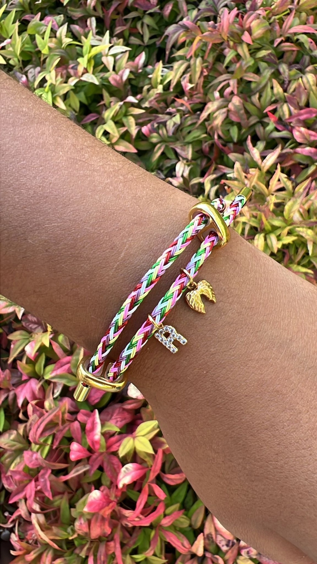 Pulseira trançada colorida com detalhes dourados e pendentes numa mão