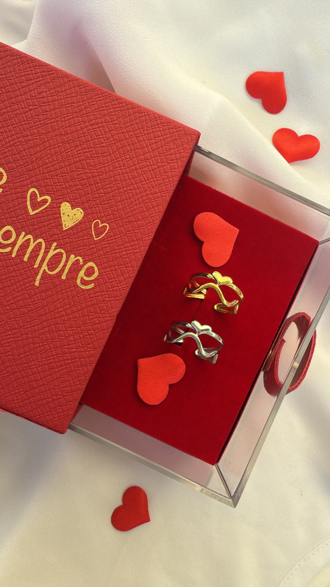Conjunto de alianças dourada e prateada com corações em caixa vermelha com tampa texto dourado