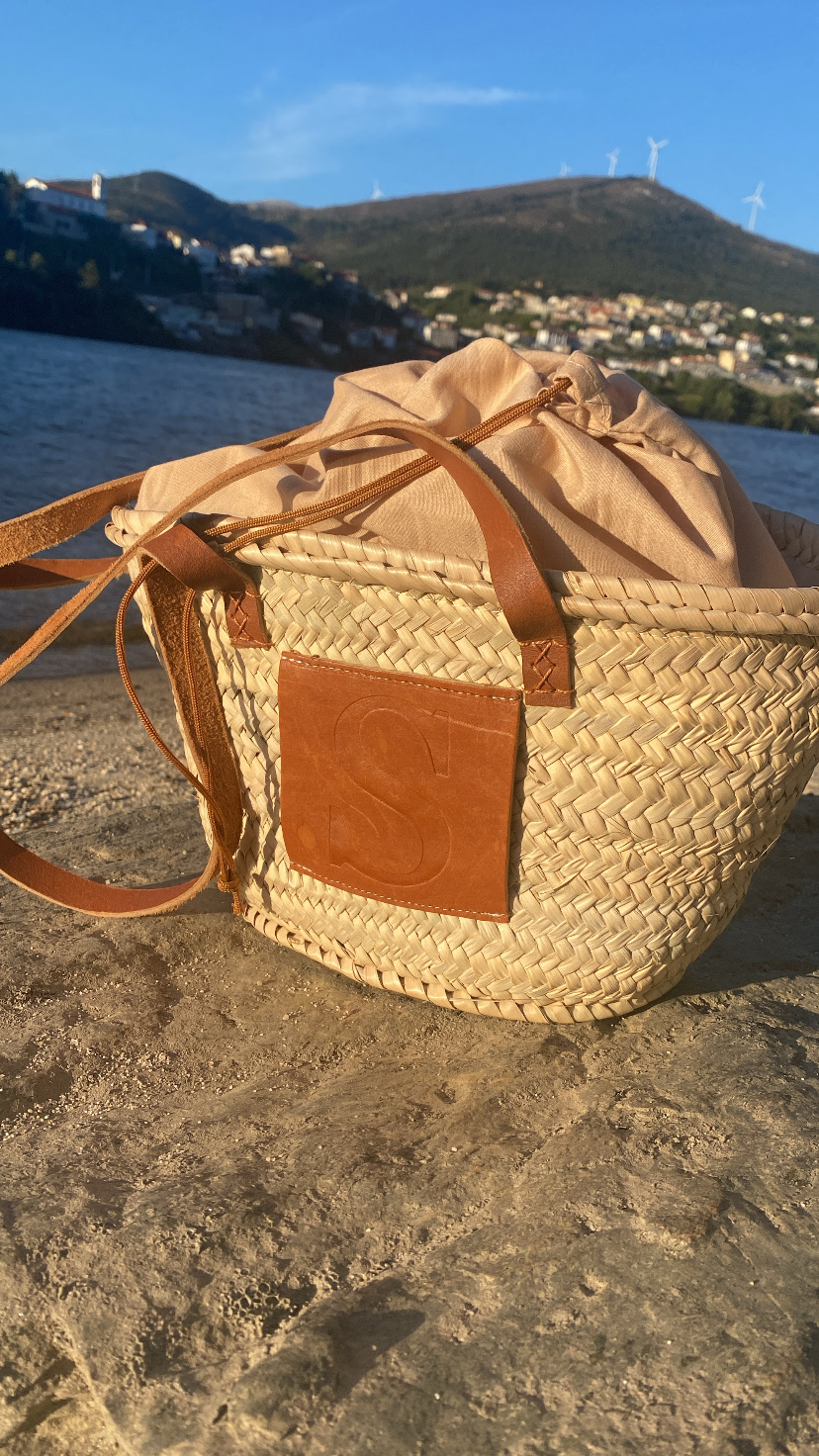 Mala de senhora trançada com bolso de couro e saco bege ao lado da água