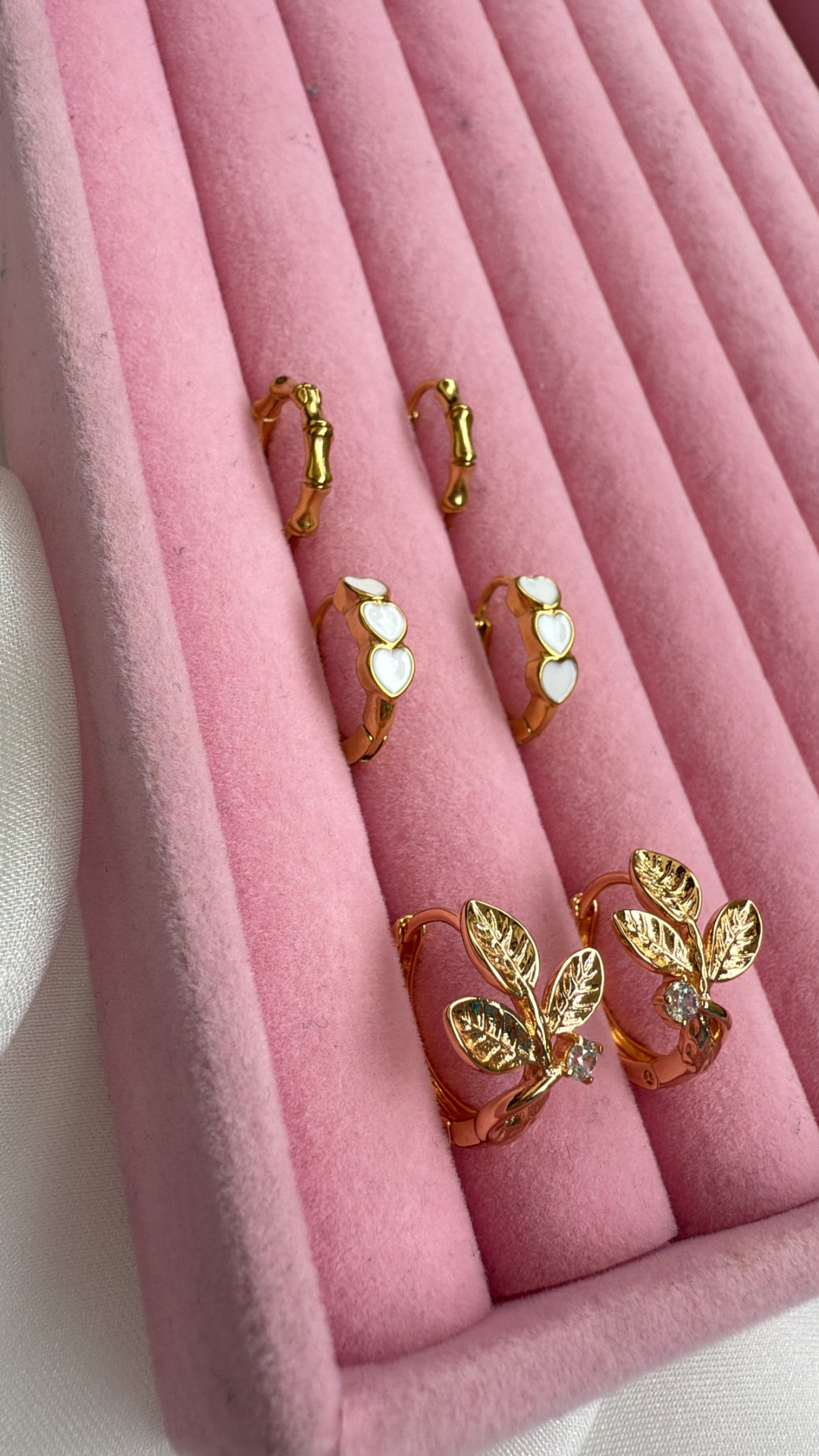 Três pares de brincos dourados numa caixa de veludo rosa