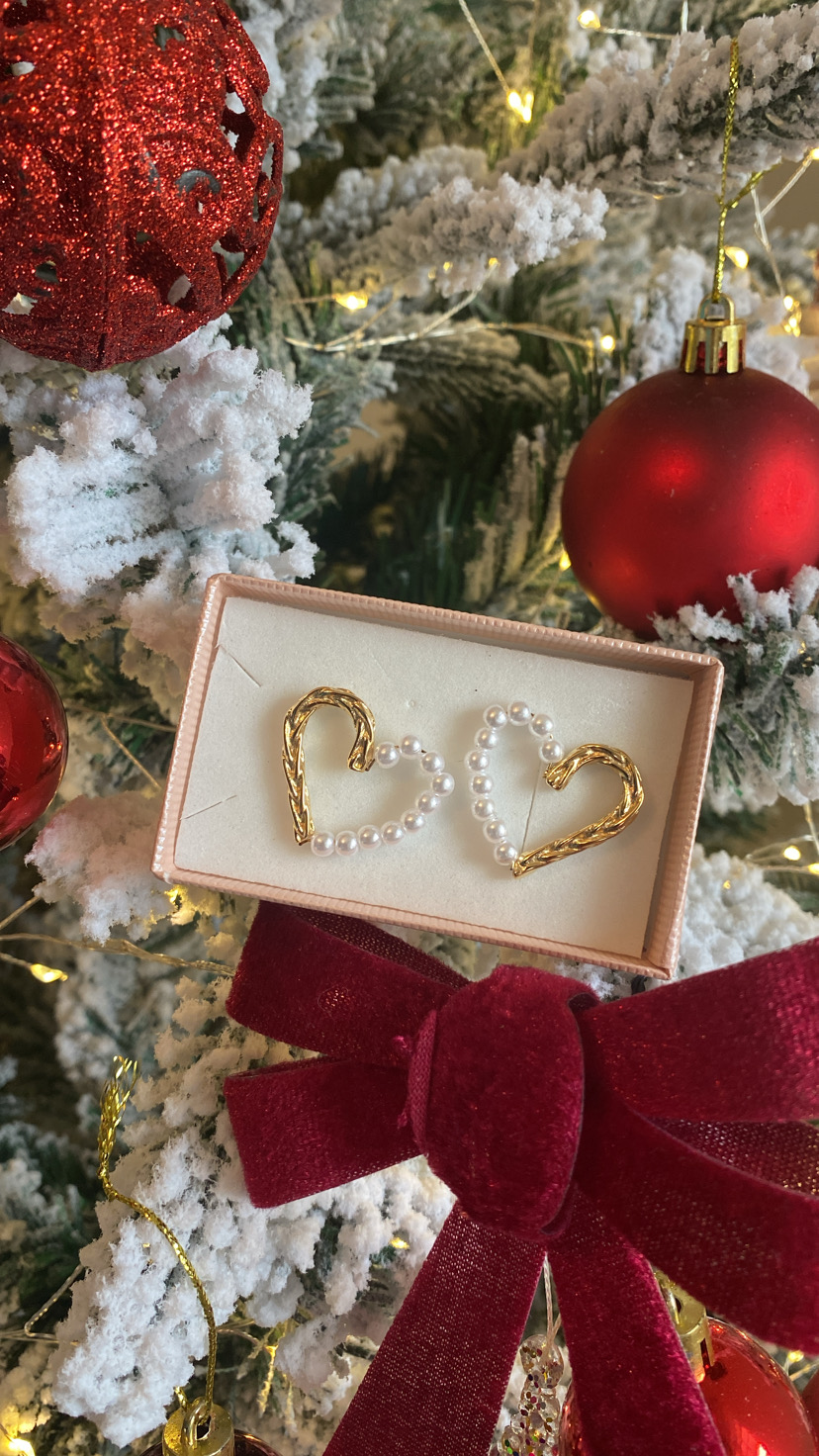 Brinco de coração dourado com pérolas em caixa sobre árvore de Natal decorada