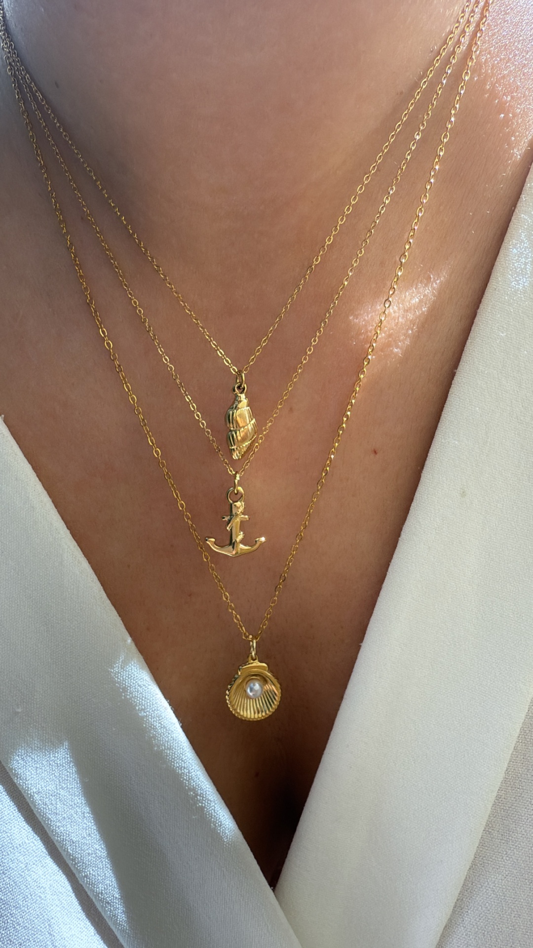 Três colares dourados com pendentes diversos em pescoço sobre blusa branca