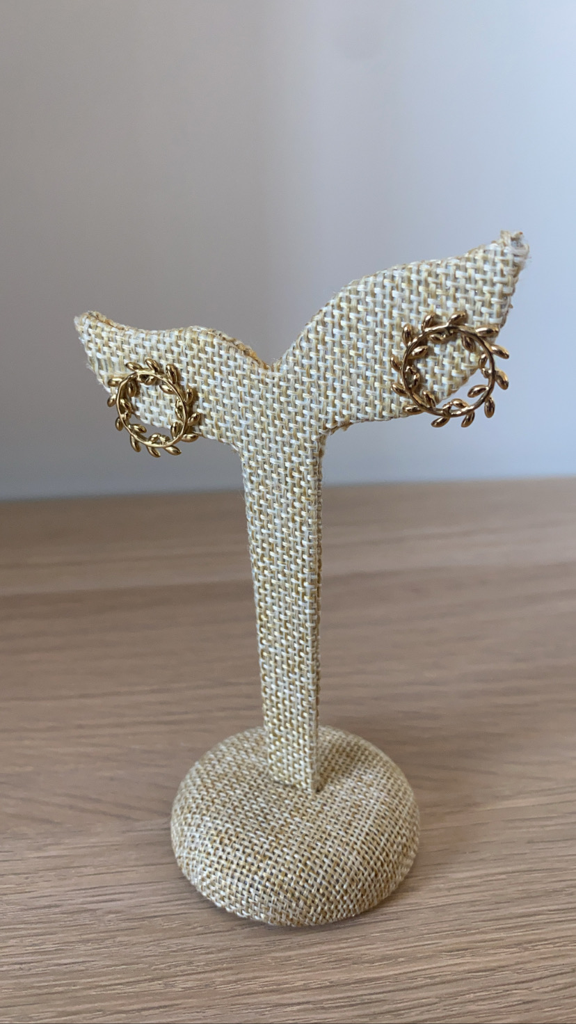 Brincos dourados com padrão de raminhos em suporte bege e fundo cinzento