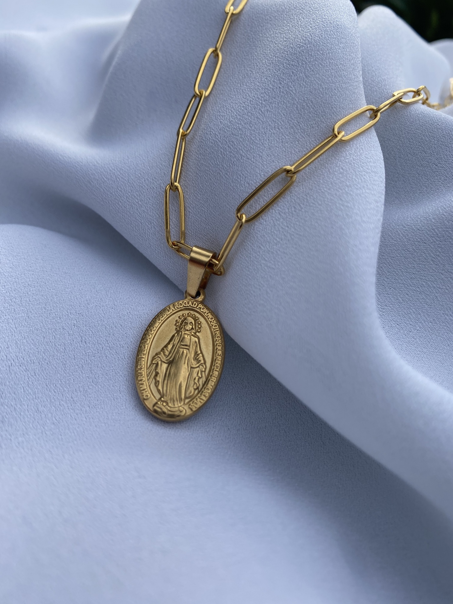 Colar dourado com pendente oval religioso sobre tecido azul claro