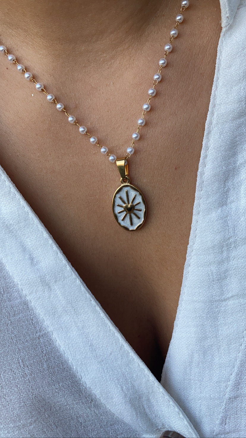 Colar com corrente de pérolas e pendente oval dourado com sol sobre roupa branca