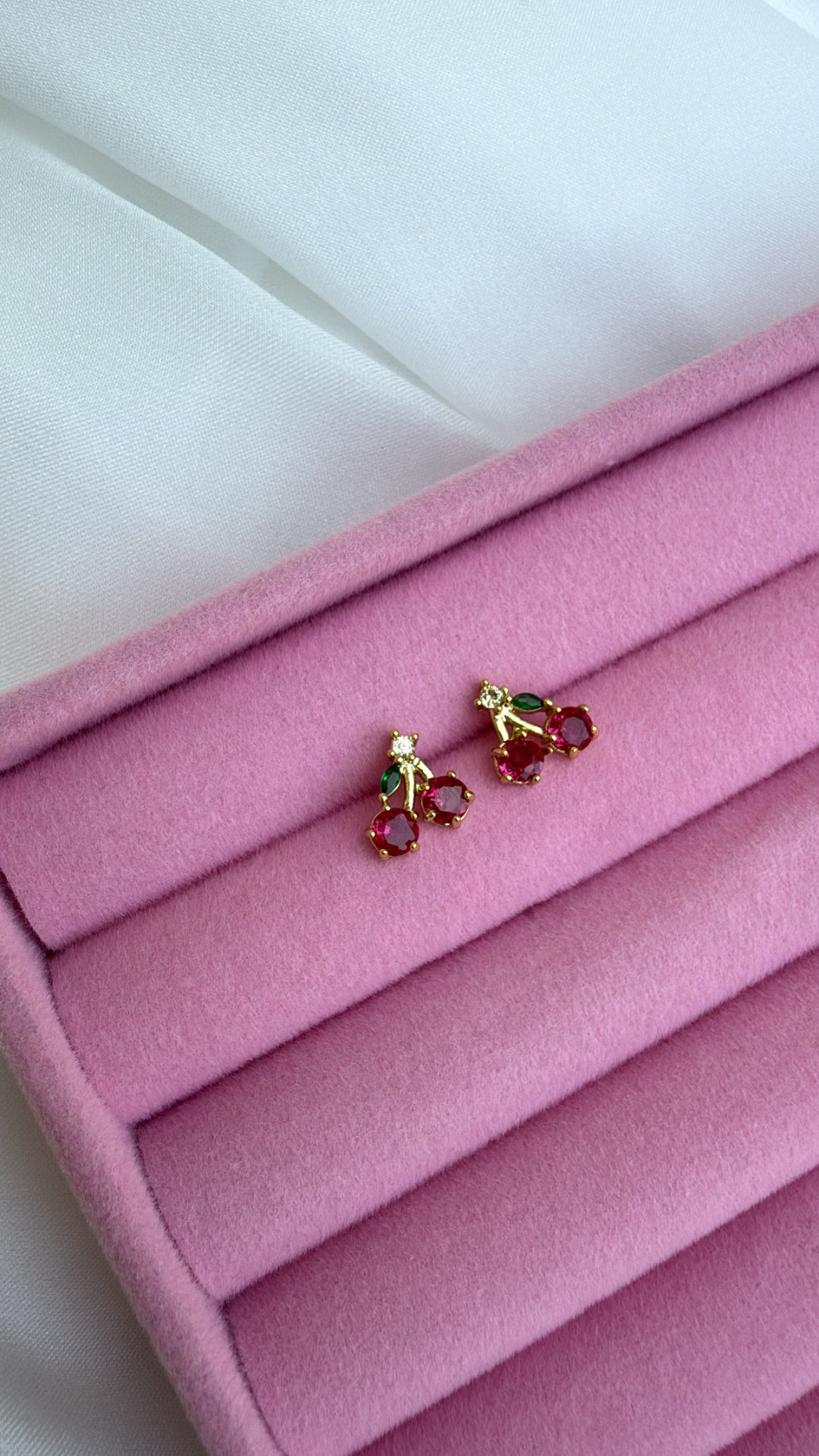 Brincos dourados com pedras vermelhas e verdes em caixa rosa
