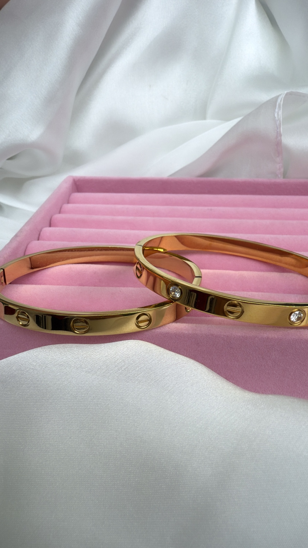 Braceletes dourados com parafusos e pedras em estojo rosa.