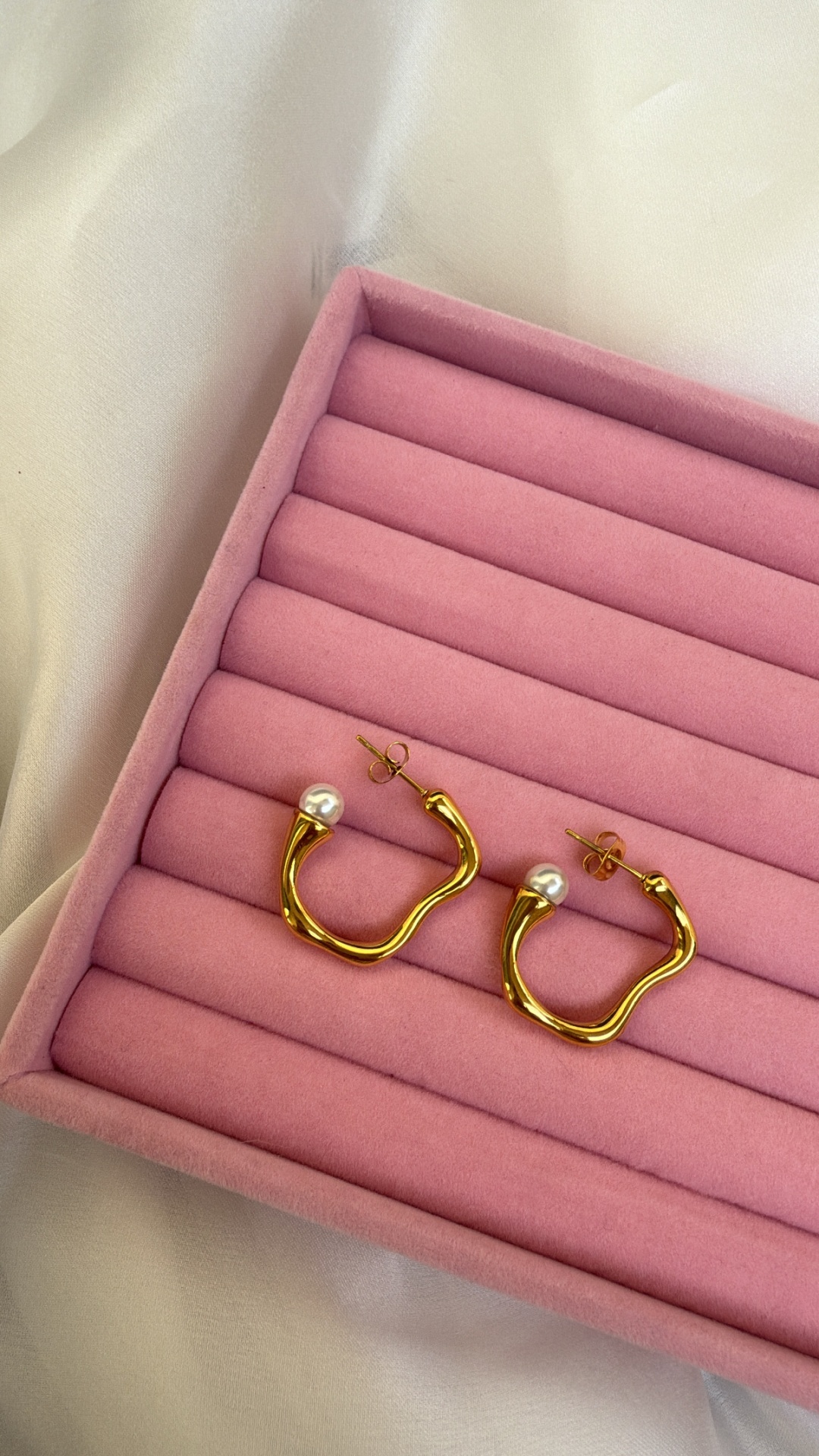 Brincos de argola dourados com pérola numa caixa rosa
