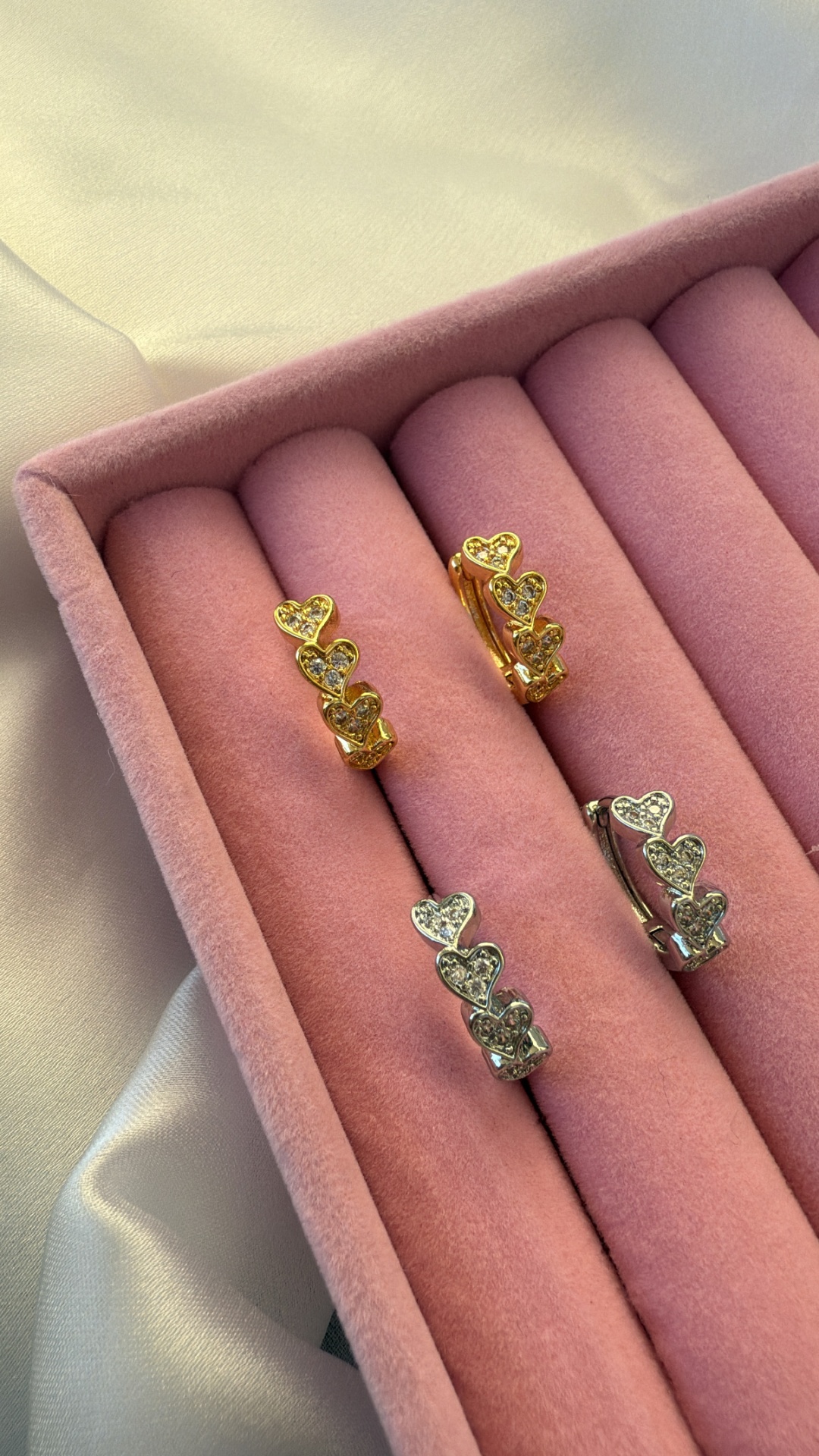 Brincos dourados e prateados com corações e pedras em caixa de veludo rosa