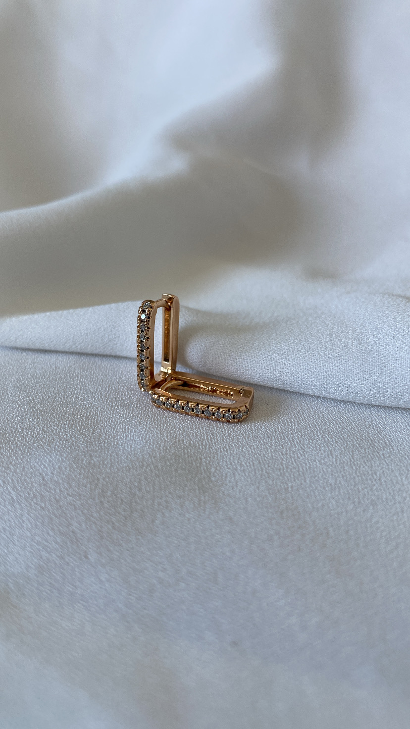 Brinco quadrado dourado com pedras brilhantes sobre tecido branco