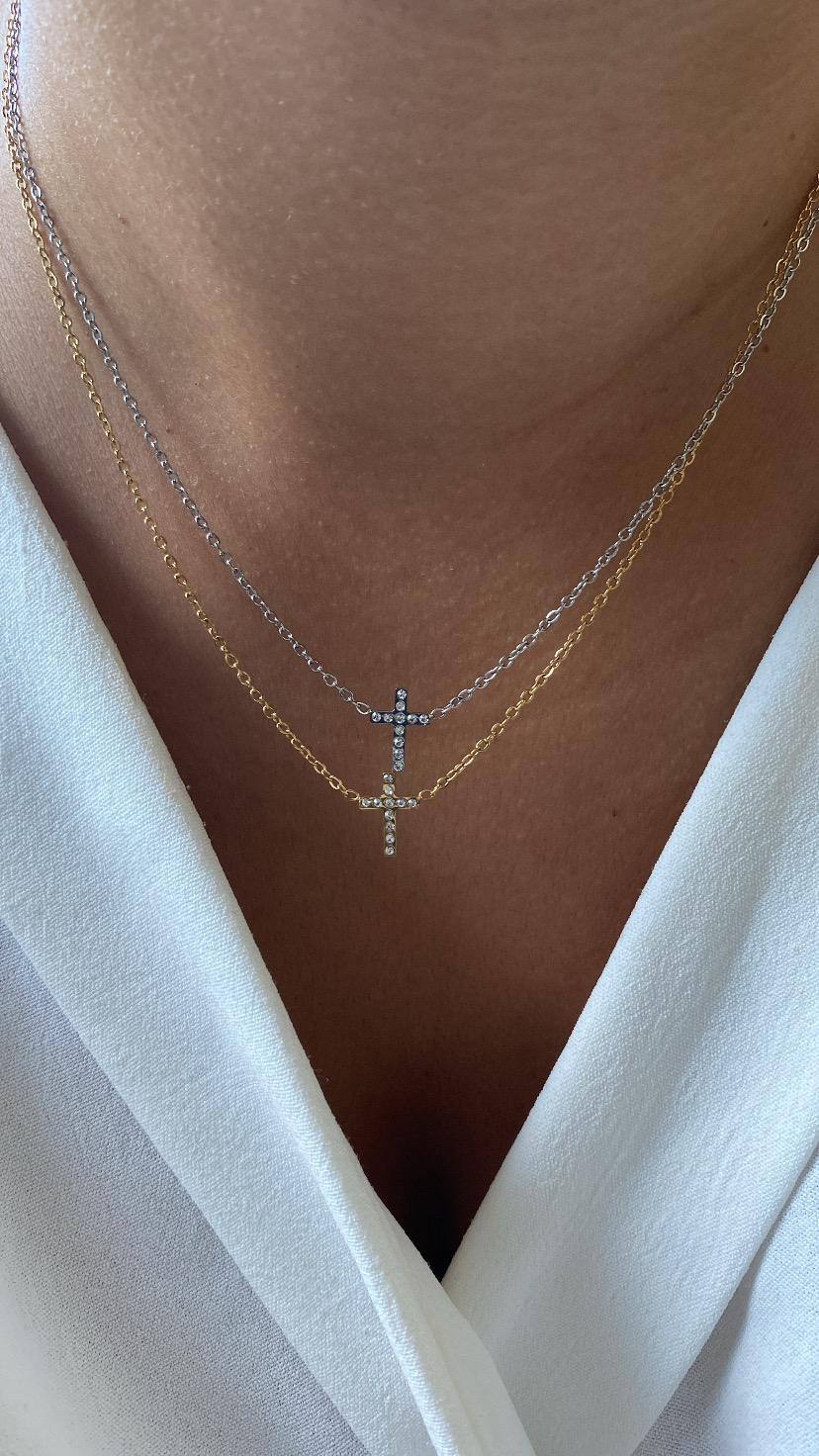 Dois colares com cruzes douradas e prateadas penduradas no pescoço de uma pessoa com roupa branca