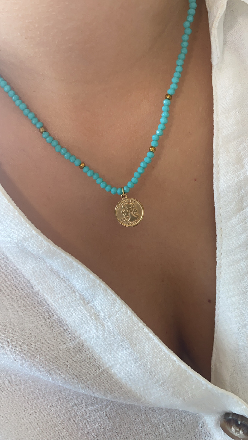 Colar azul com contas e pendente dourado num pescoço com camisa branca