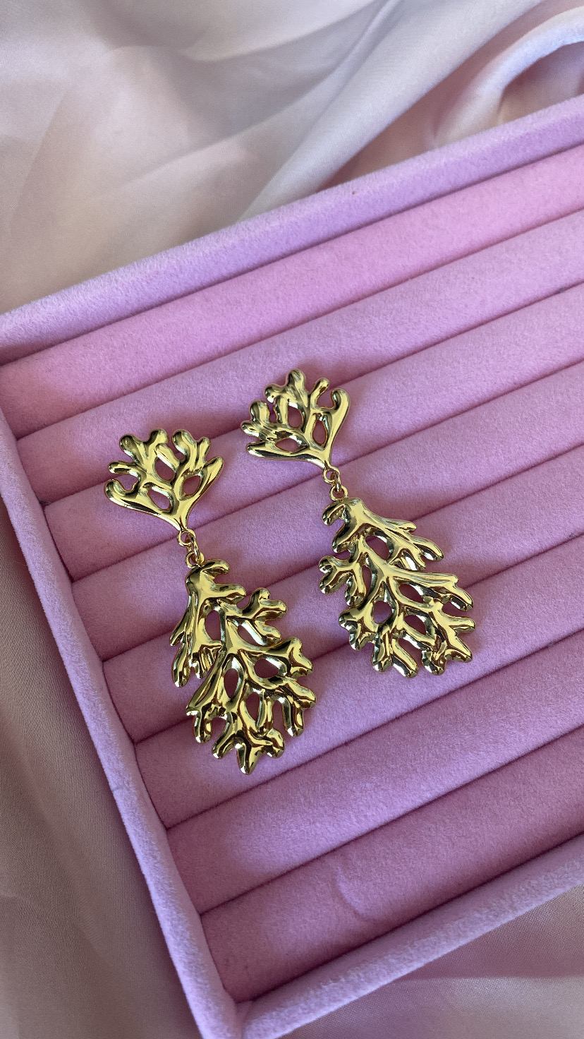 Brincos dourados com design de ramos sobre almofada rosa