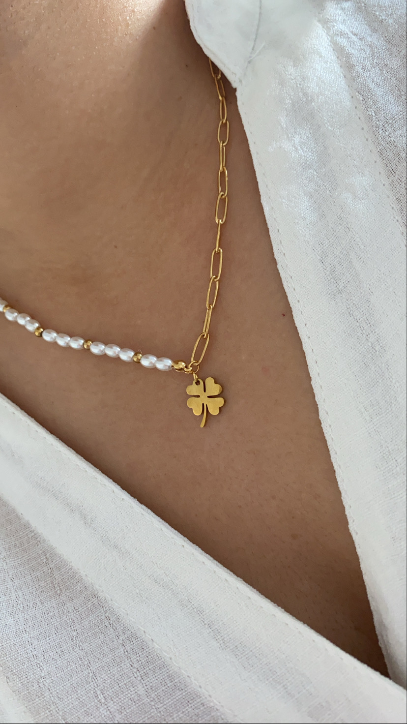 Colar feminino com correntes douradas, pérolas brancas e pendente de trevo dourado sobre pele e camisa branca