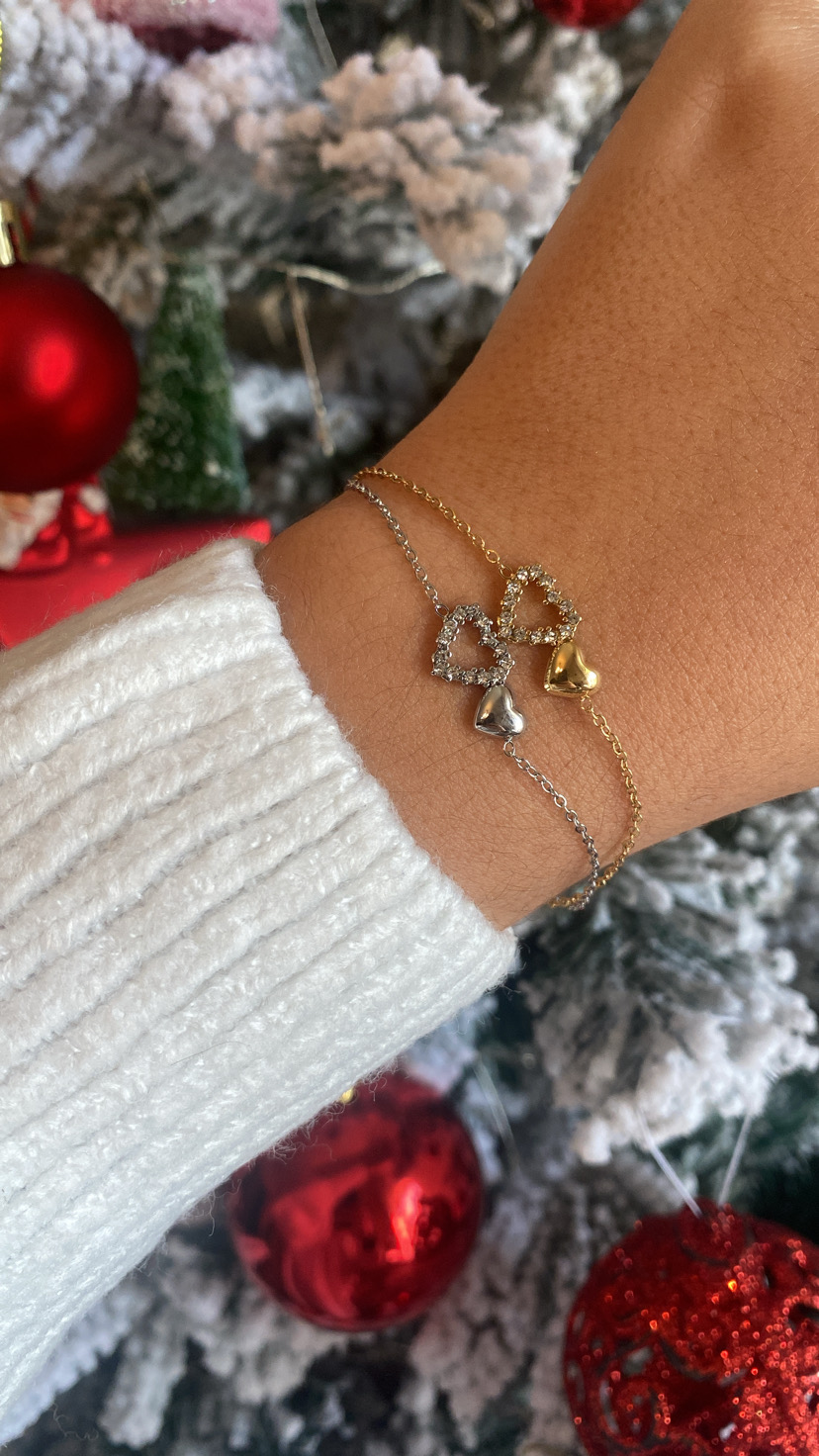 Pulso com pulseiras dourada e prateada com corações e árvore de Natal decorada ao fundo