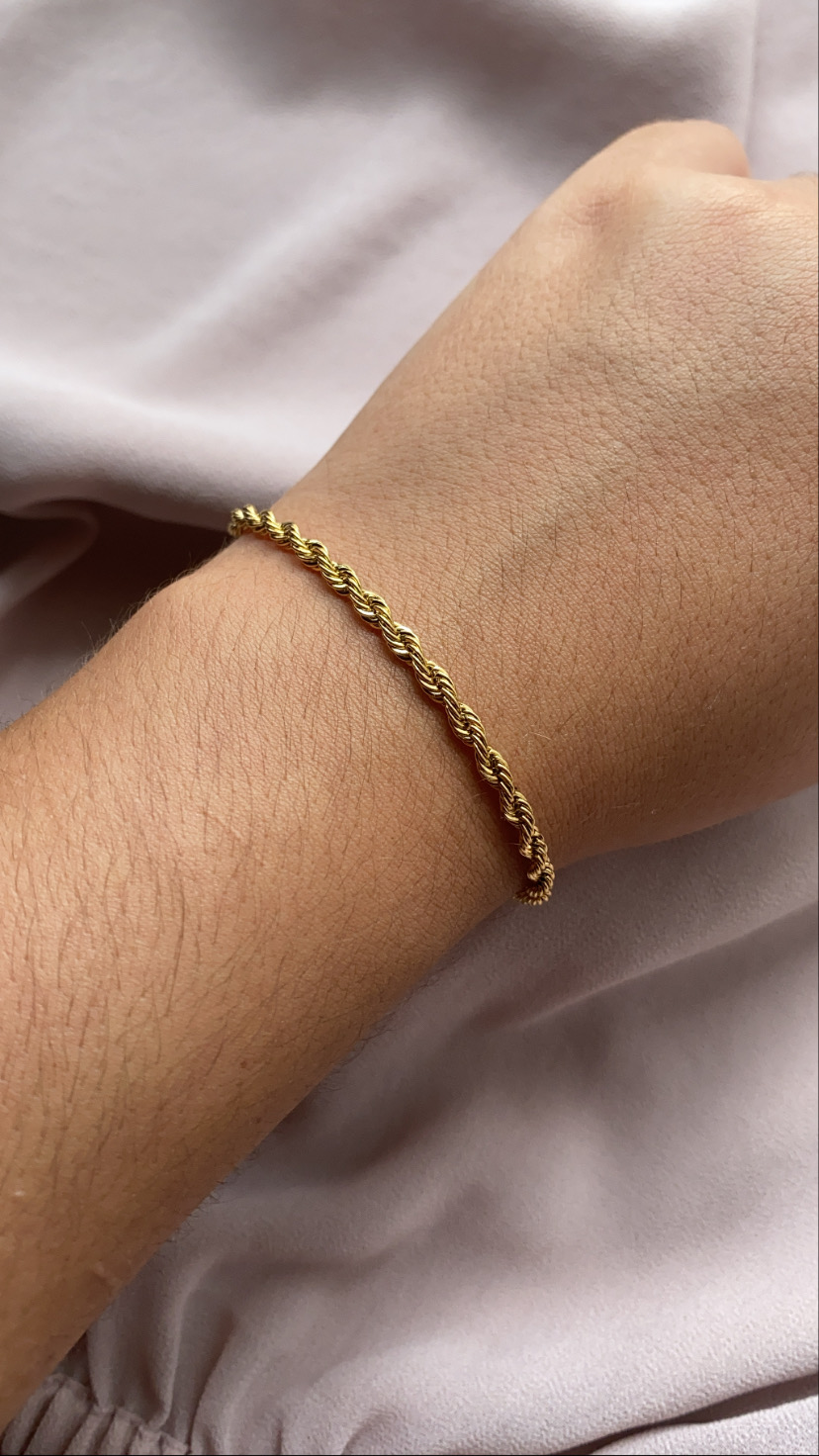 Pulseira dourada fina com design torcido no pulso