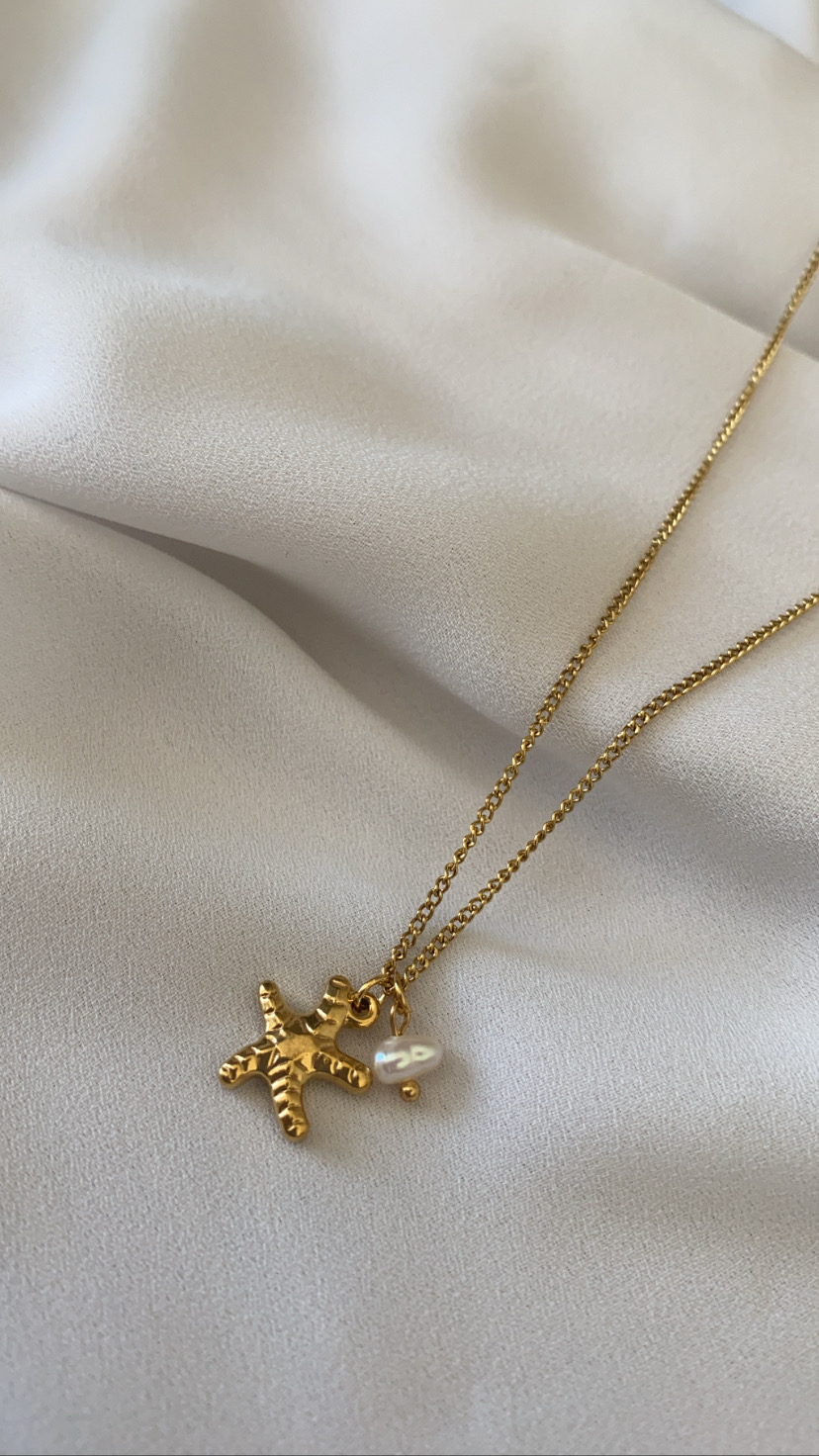 Colar dourado com pendente figura humana e pérola sobre tecido branco