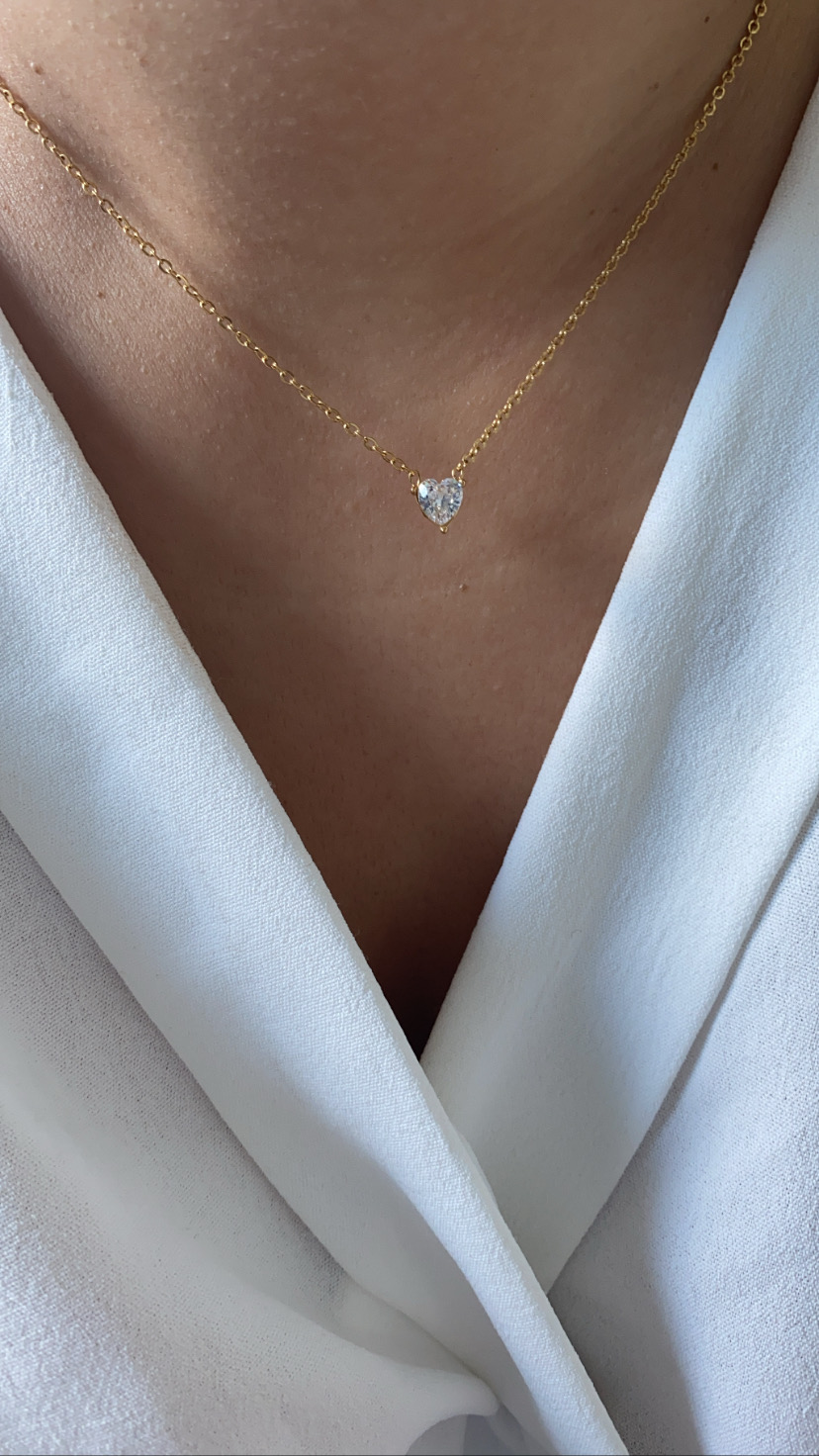 Colar dourado com pendente de coração brilhante sobre blusa branca