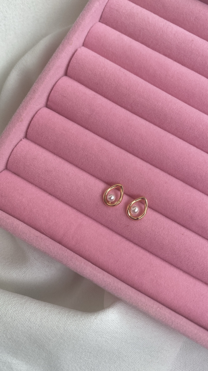 Brincos dourados com pérolas numa almofada rosa de veludo