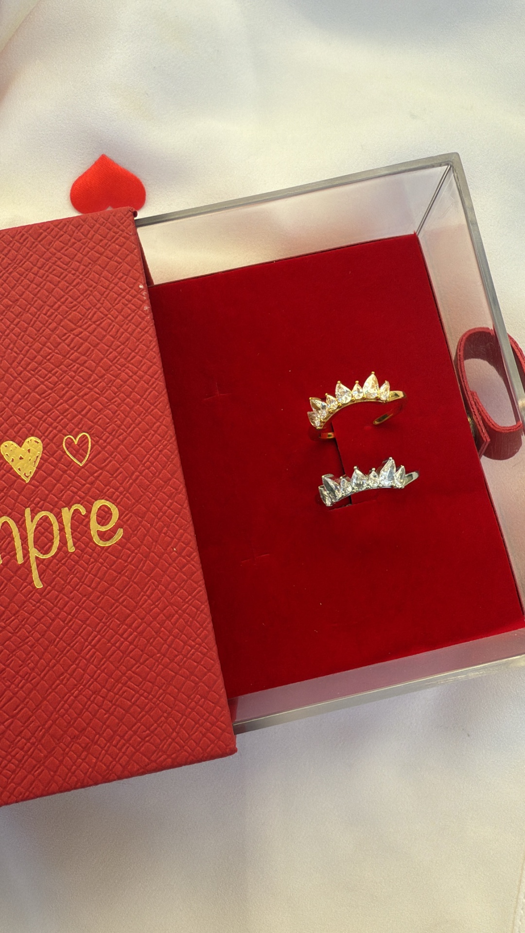 Brincos dourado e prateado com pedras em caixa vermelha texturada com texto 'sempre'