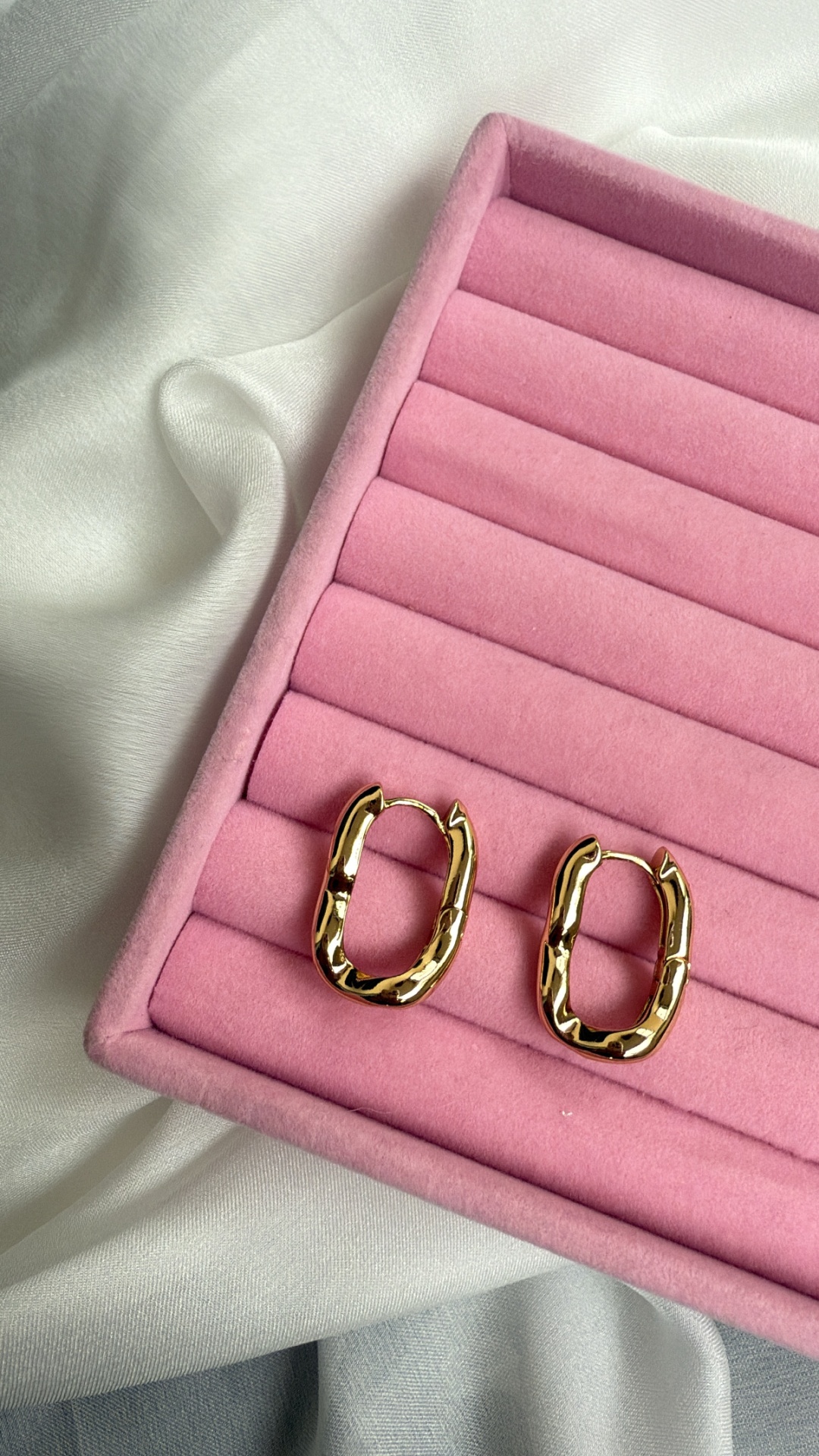 Par de brincos oval dourados em estojo rosa sobre tecido branco