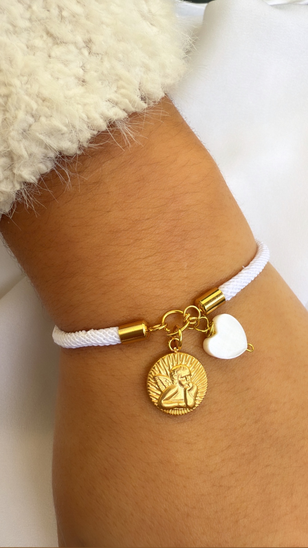Pulseira branca com pendentes dourado e coração branco num pulso