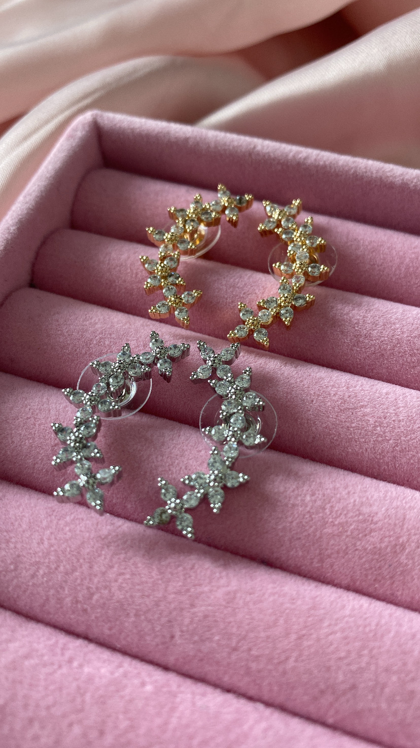 Dois pares de brincos meia-lua dourados e prateados com flores e pedras em caixa rosa.