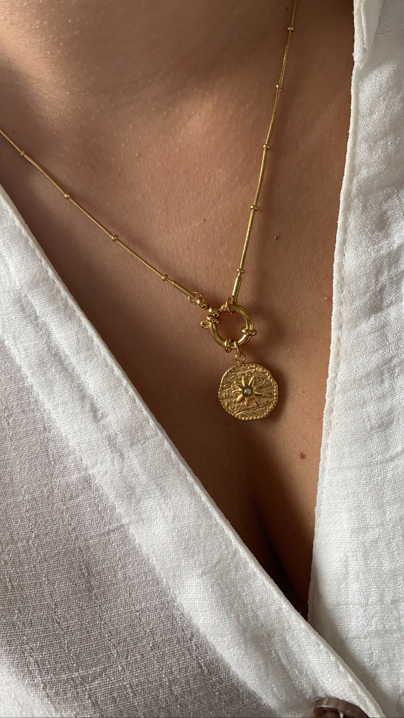 Colar dourado com pendente redondo texturado usado com vestido branco