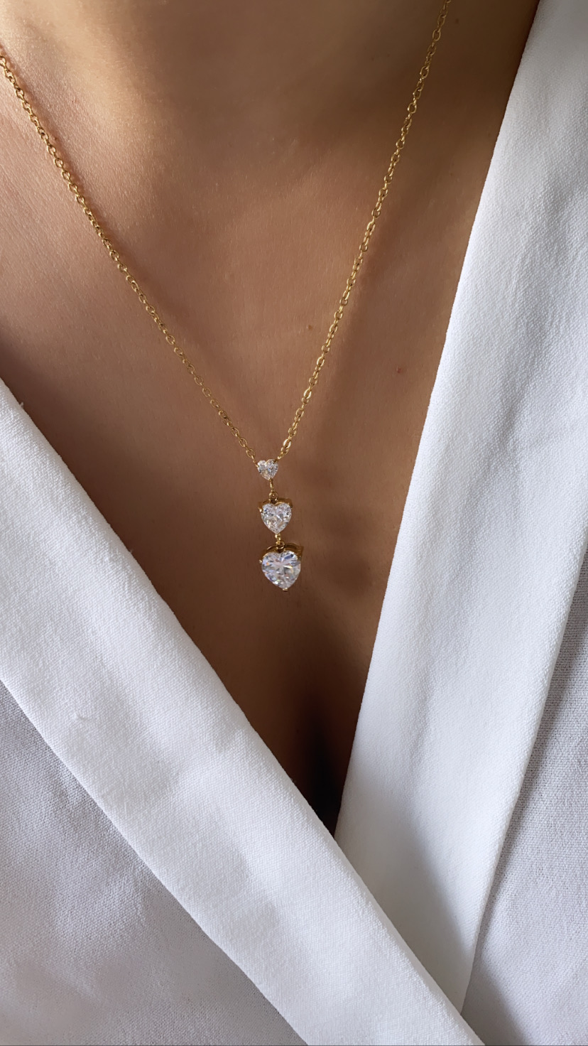 Colar dourado com três corações brilhantes sobre roupa branca