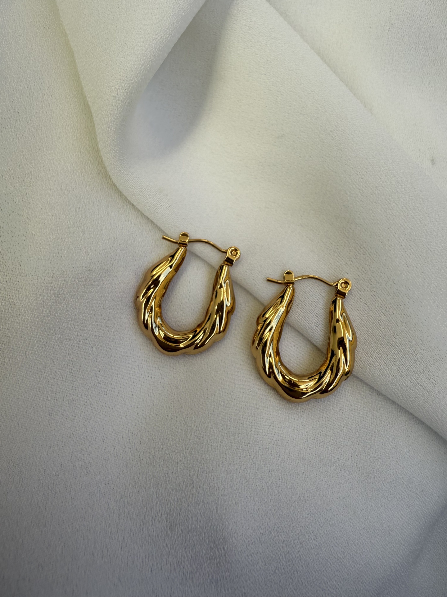 Brincos dourados em forma de argola sobre tecido branco