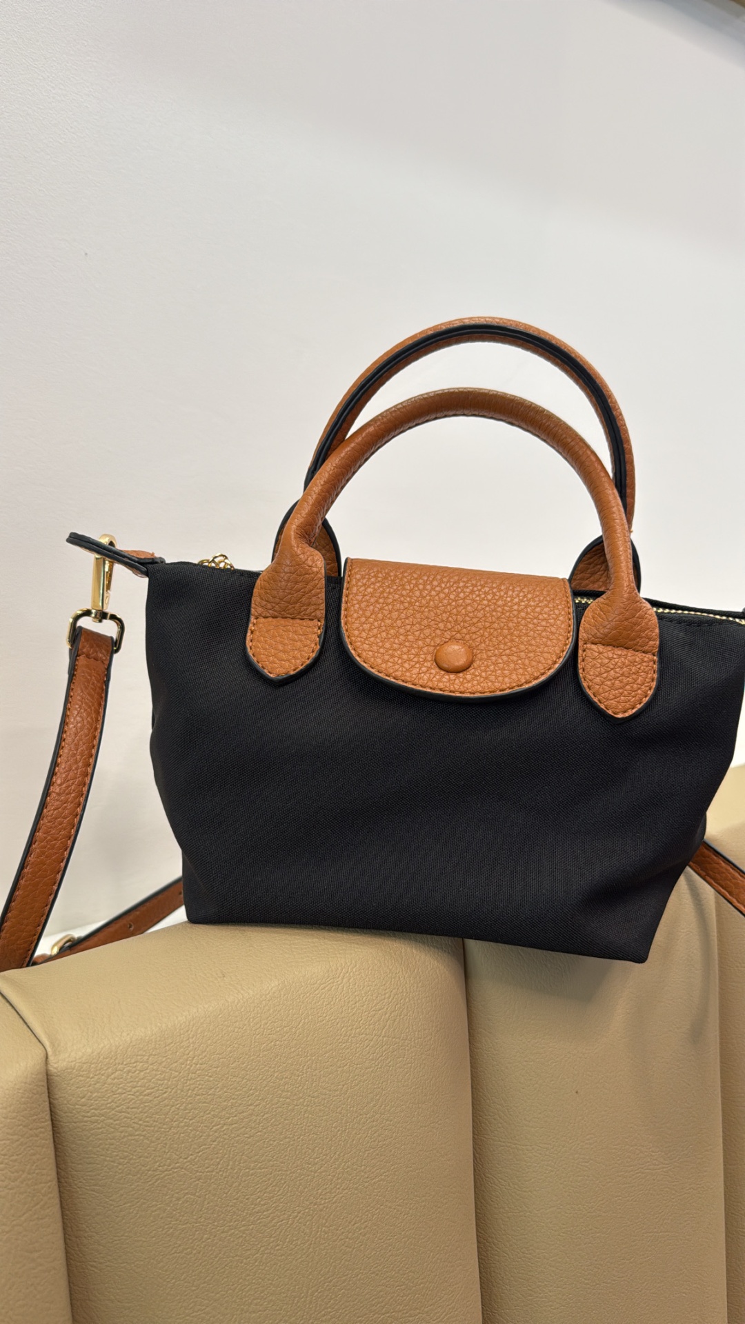 Saco de mão preto com detalhes castanhos em pele, apoiado num sofá bege