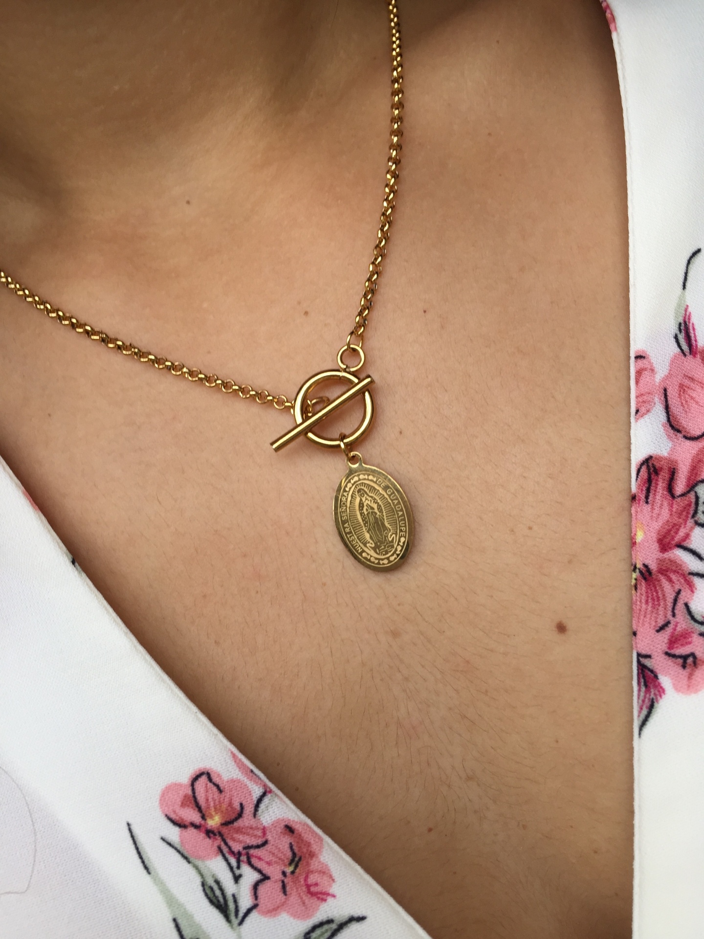 Colar dourado com pendente de medalha religiosa em corpo com vestido branco floral