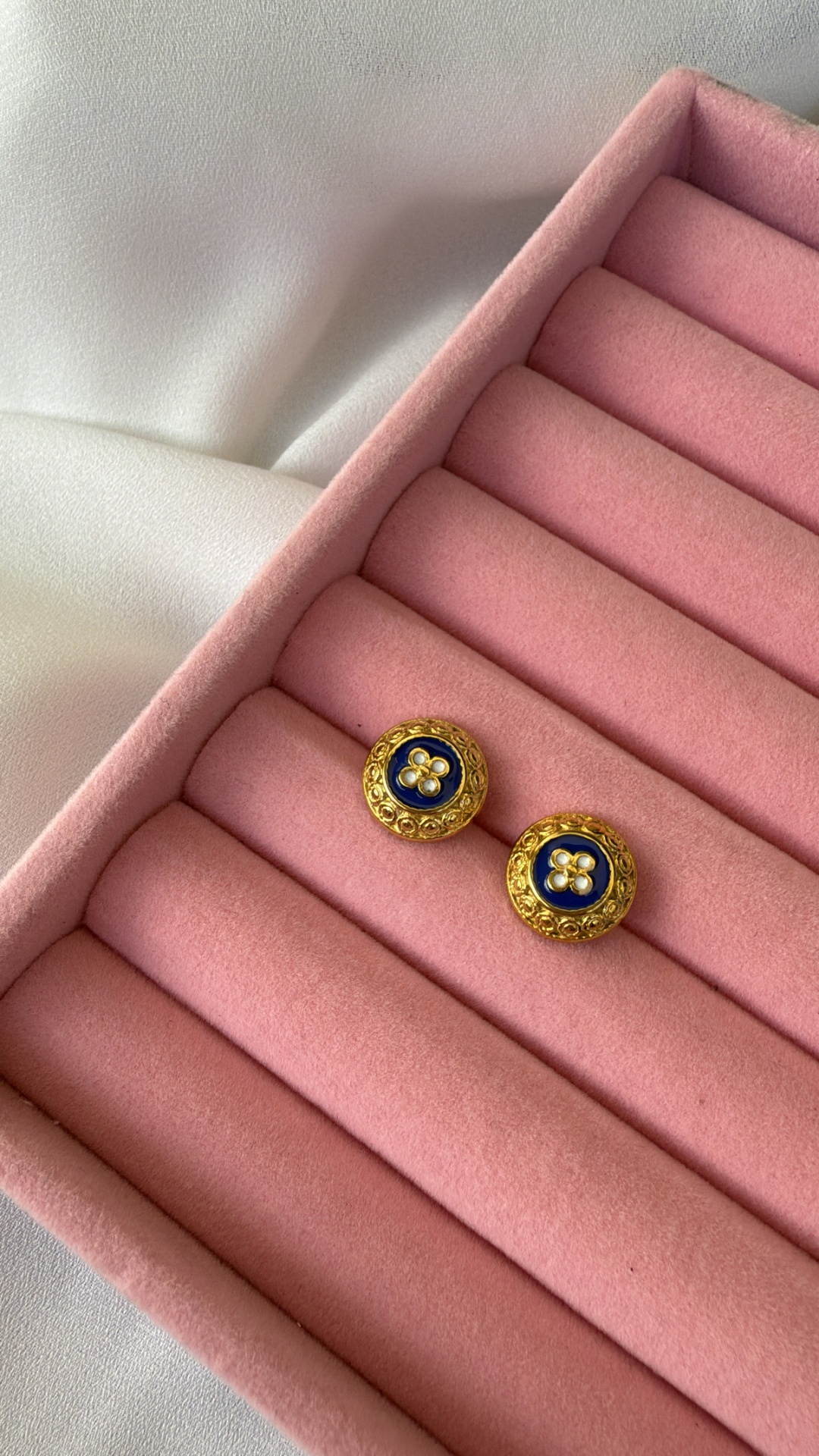 Par de botões dourados com interior azul e detalhe floral branco numa caixa rosa aveludada