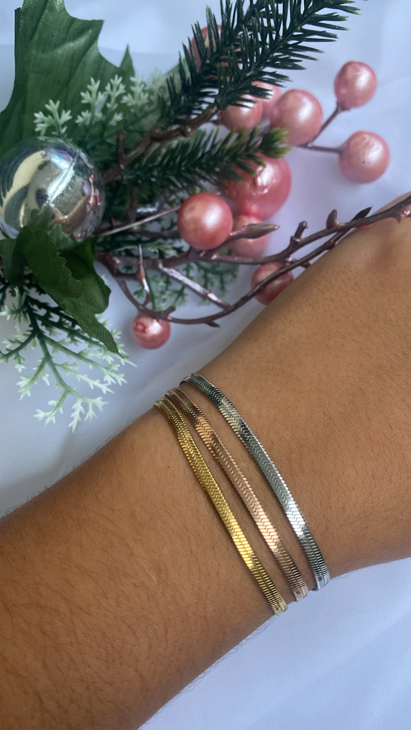 Pulseiras finas dourada, rosé e prateada no pulso com decoração floral ao fundo