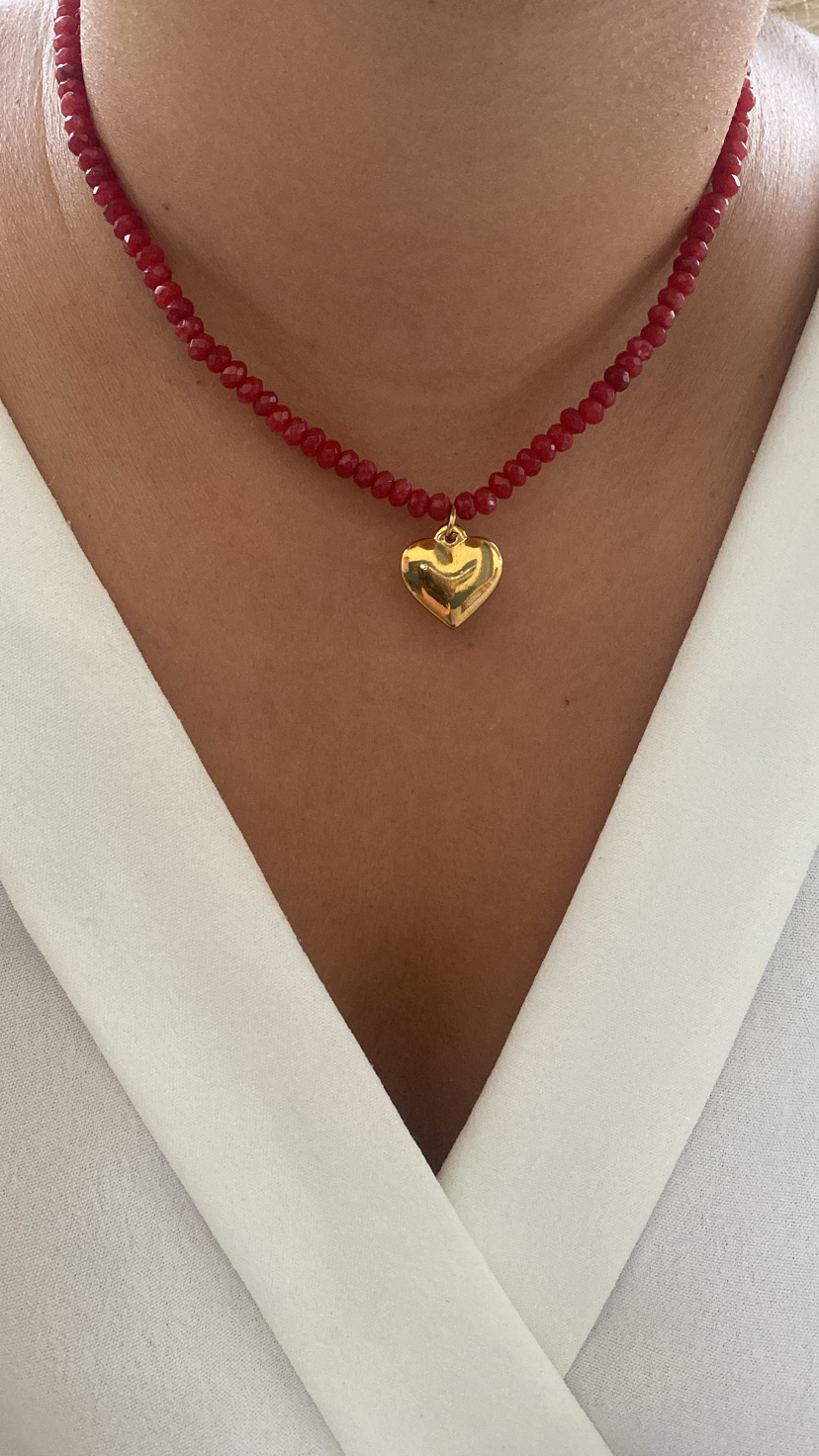 Colar vermelho com pendente coração dourado no pescoço de mulher com roupa branca